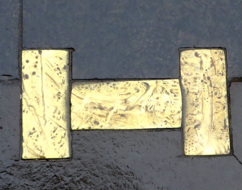 Three Brass plates set in the ground in the shape of the letter aitch