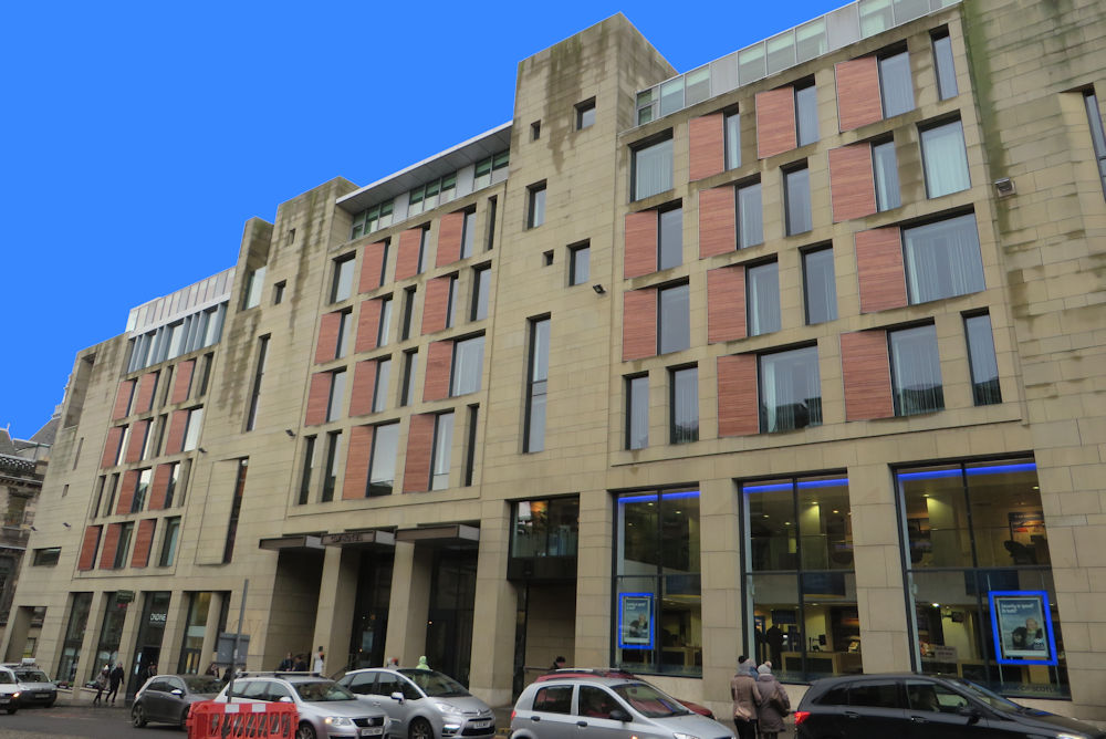 A modern hotel building, built from sandstone with red detailing on the frontage.