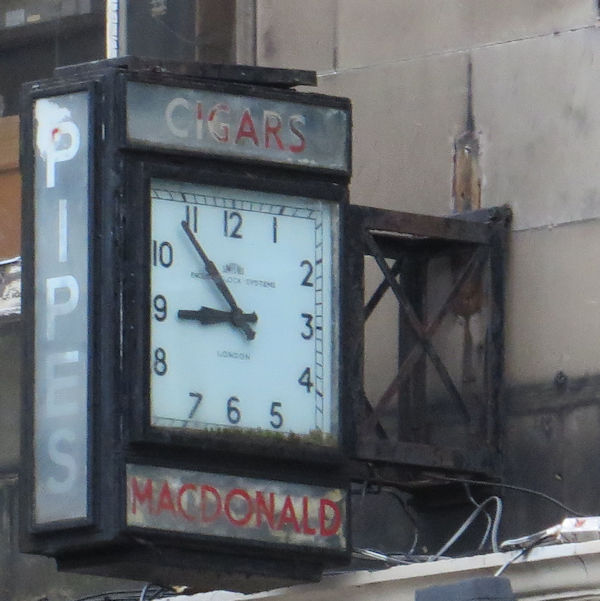 An old square clock attached to the front of a building. The hands are stilled at five minutes to nine